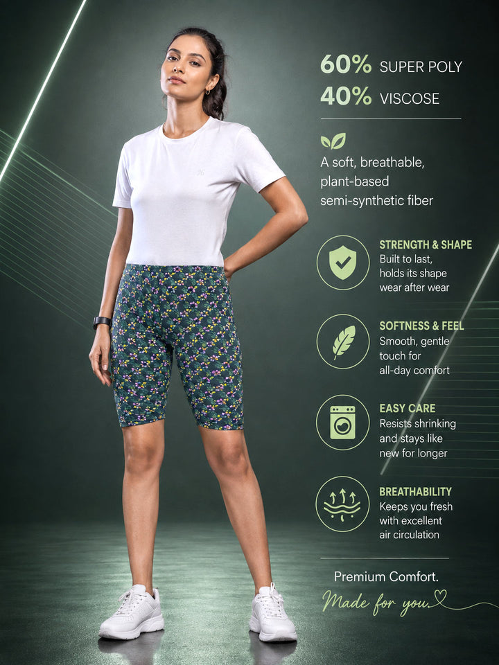 A woman modeling patterned athletic biker shorts with a white t-shirt and white sneakers, set against a dark green background with product feature text and icons detailing the fabric composition and benefits.