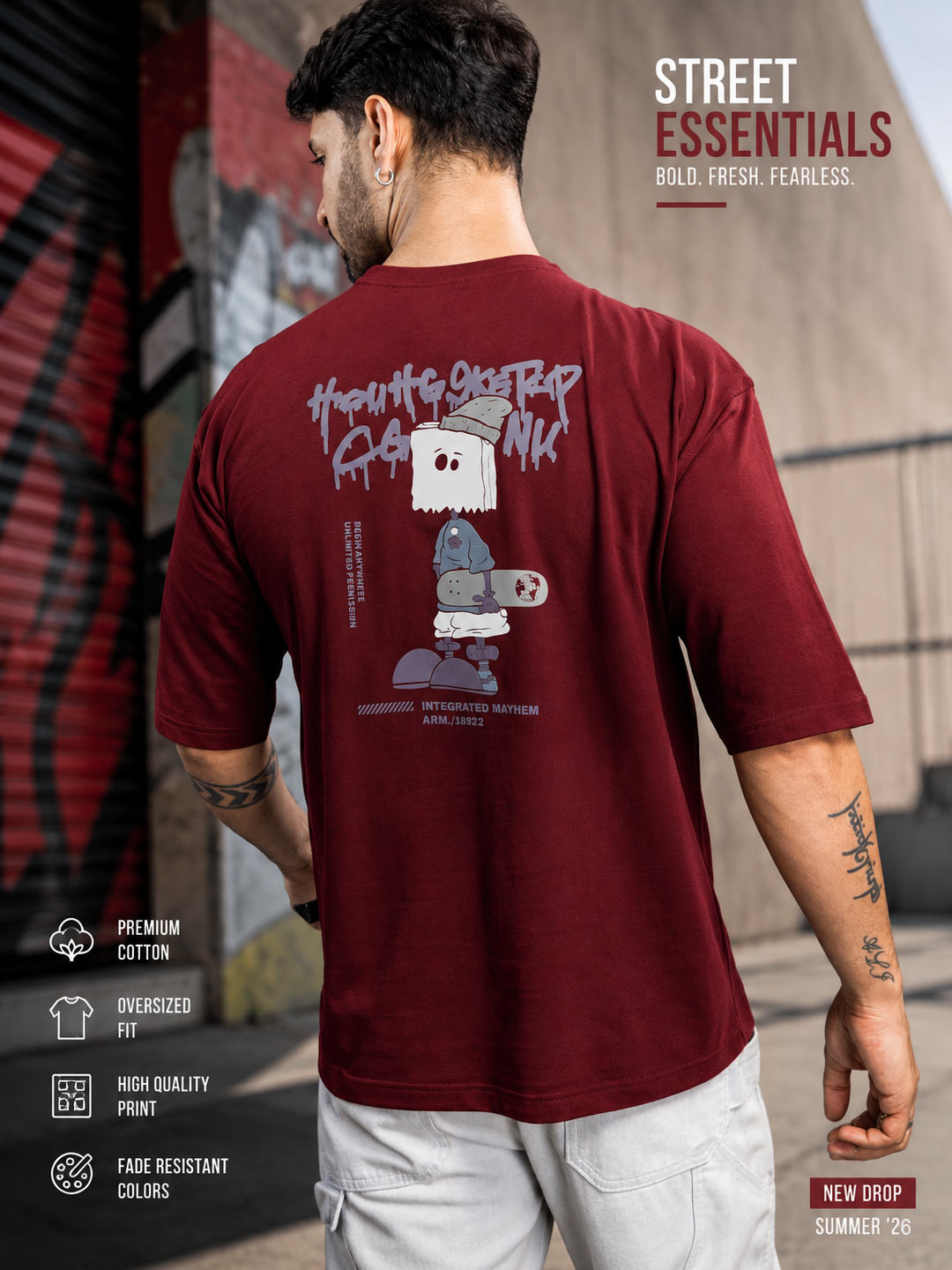 A man wearing a maroon short-sleeve t-shirt with a large cartoon graphic on the back, shown from behind in an outdoor urban setting. The graphic features a white ghost and a blue robot holding a game controller.