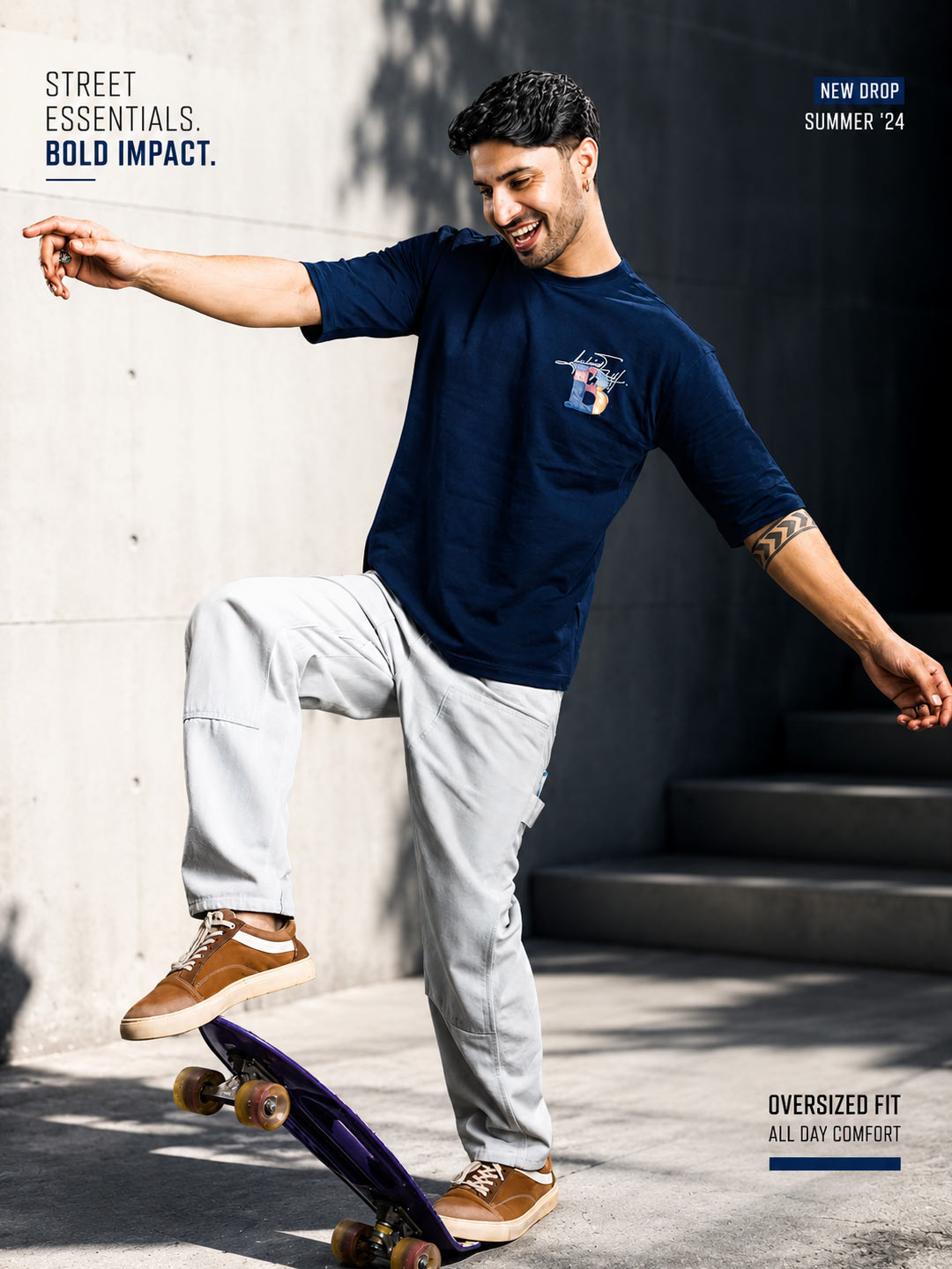A man skateboarding outdoors wearing a navy blue oversized short-sleeve t-shirt with a small white and red graphic on the left chest, light gray sweatpants, and brown sneakers.