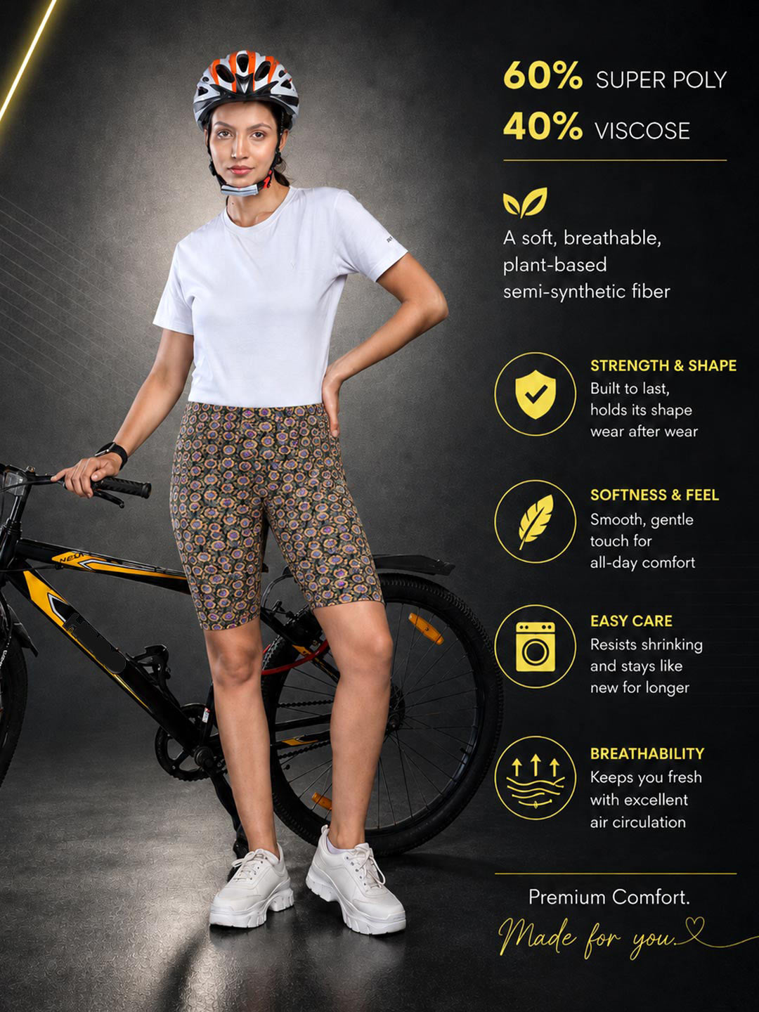 A woman wearing a bicycle helmet and a white t-shirt stands next to a bicycle, modeling patterned biker shorts. The image includes text overlays detailing the fabric composition and product features.