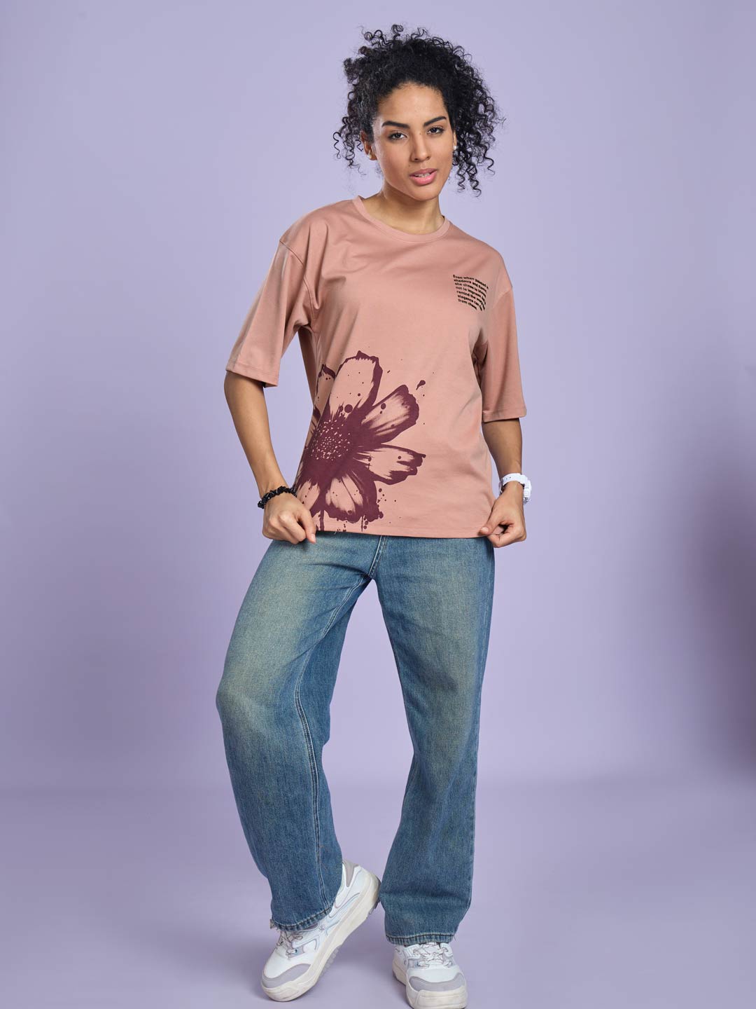 Woman wearing a pink t-shirt with a butterfly design and blue jeans on a light purple background