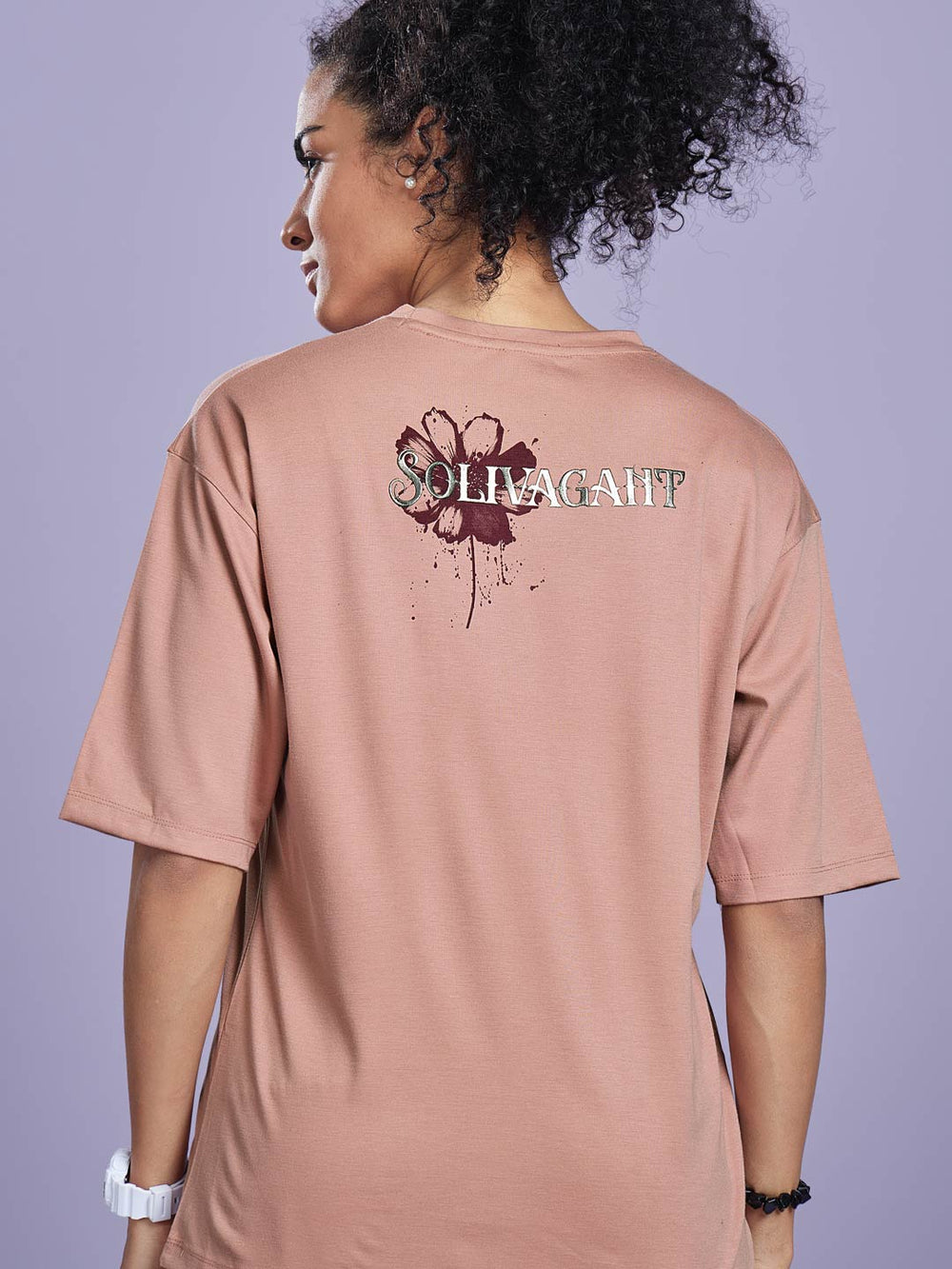 Person wearing a pink t-shirt with a floral design and text on the back against a light purple background