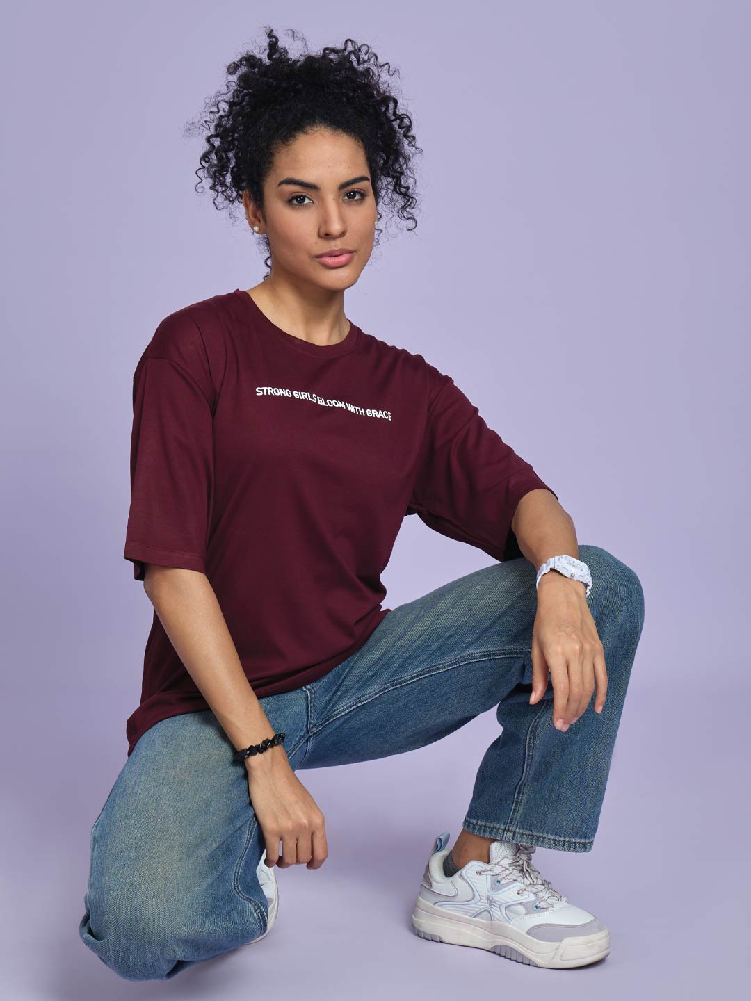 Woman wearing a maroon t-shirt and blue jeans on a light purple background