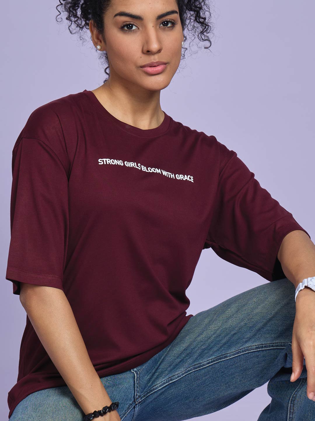 Woman wearing a maroon t-shirt with text, sitting against a light purple background