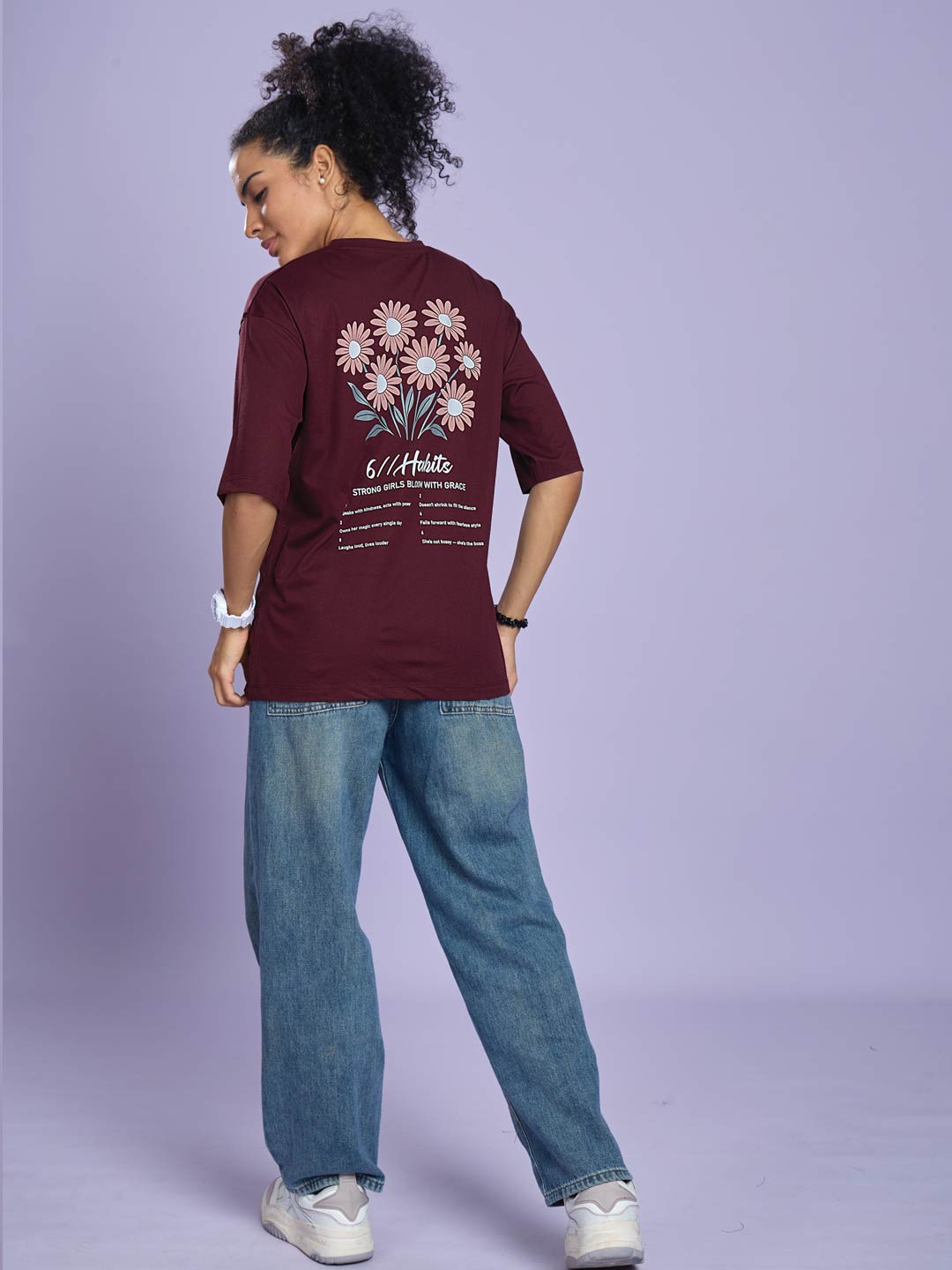 Person wearing a maroon t-shirt with floral design and text on a light purple background