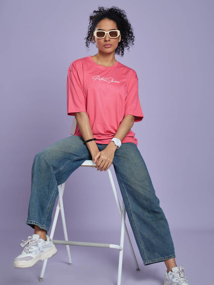 Person wearing a pink t-shirt and blue jeans sitting on a white stool against a purple background