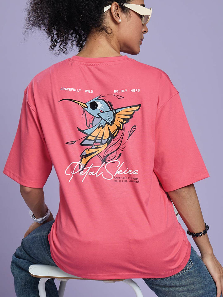 Person wearing a pink t-shirt with a colorful design and text on the back, sitting against a light purple background.